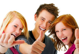 Portrait of three young teenagers laughing and giving the thumbs-up sign.